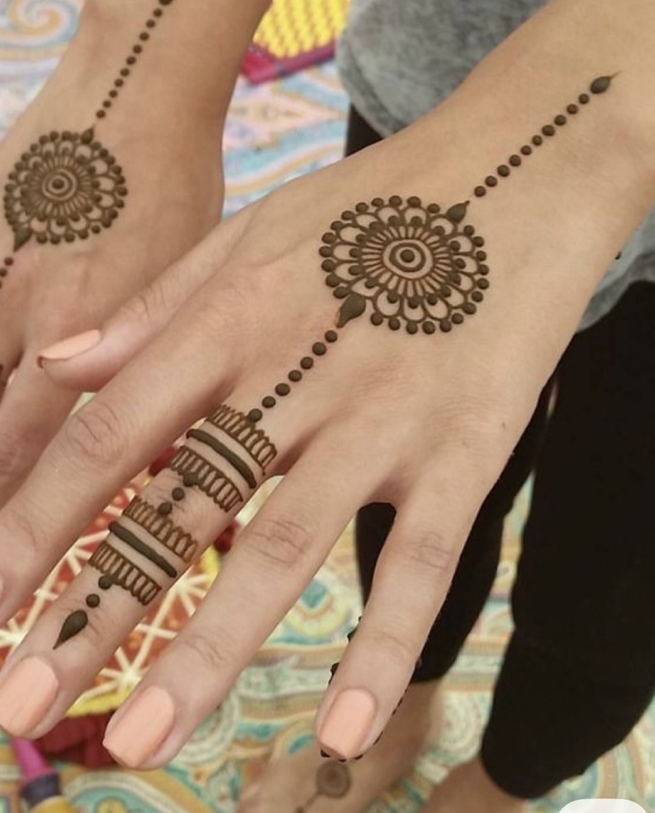 Matching mandala henna on both hands with beaded finger designs at a festival