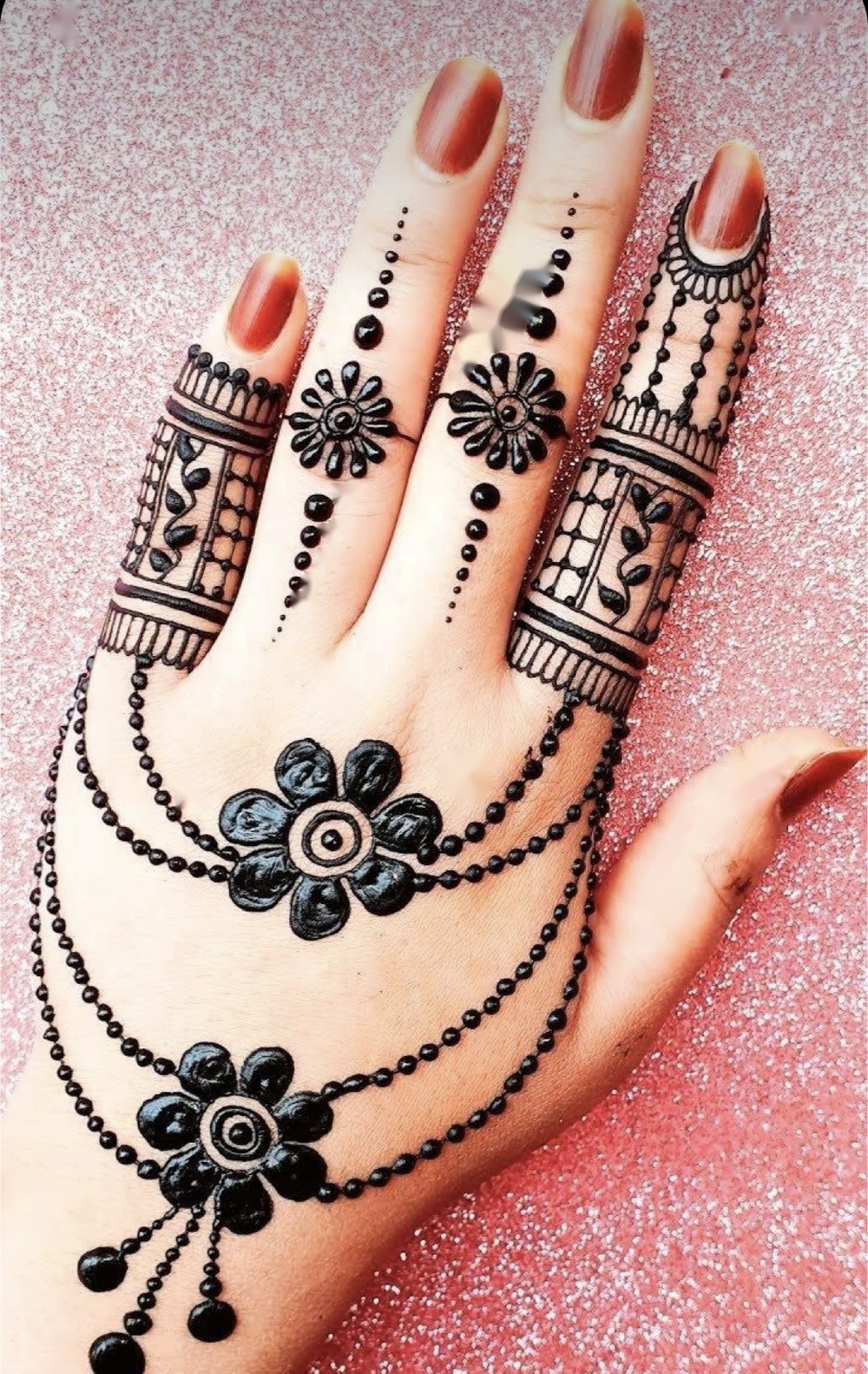 Black henna floral and beaded bracelet-style design on the back of a hand